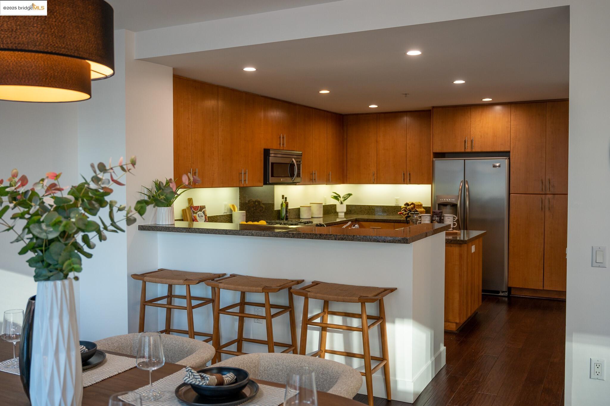 438 West Grand Avenue, Unit 422 Oakland, CA 94612 - Photo 44 of 52 Kitchen featuring a breakfast bar area, brown cabinets, a peninsula, dark stone countertops, and recessed lighting