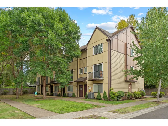 a view of a white house next to a yard with big trees