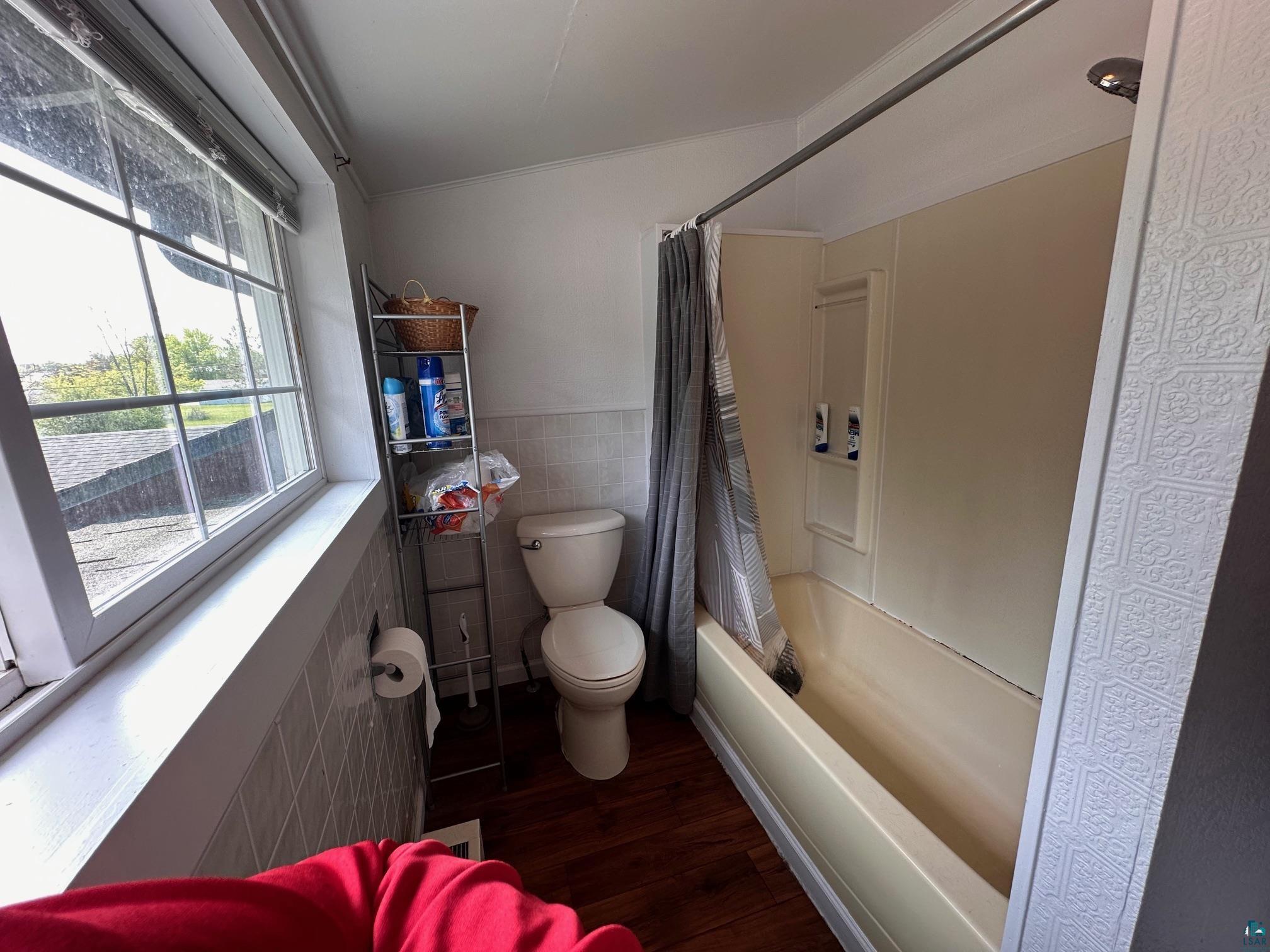 1601 4th Avenue International Falls, MN 56649 - Photo 30 of 50 Bathroom featuring tile walls, toilet, wood finished floors, shower / tub combo with curtain, and wainscoting