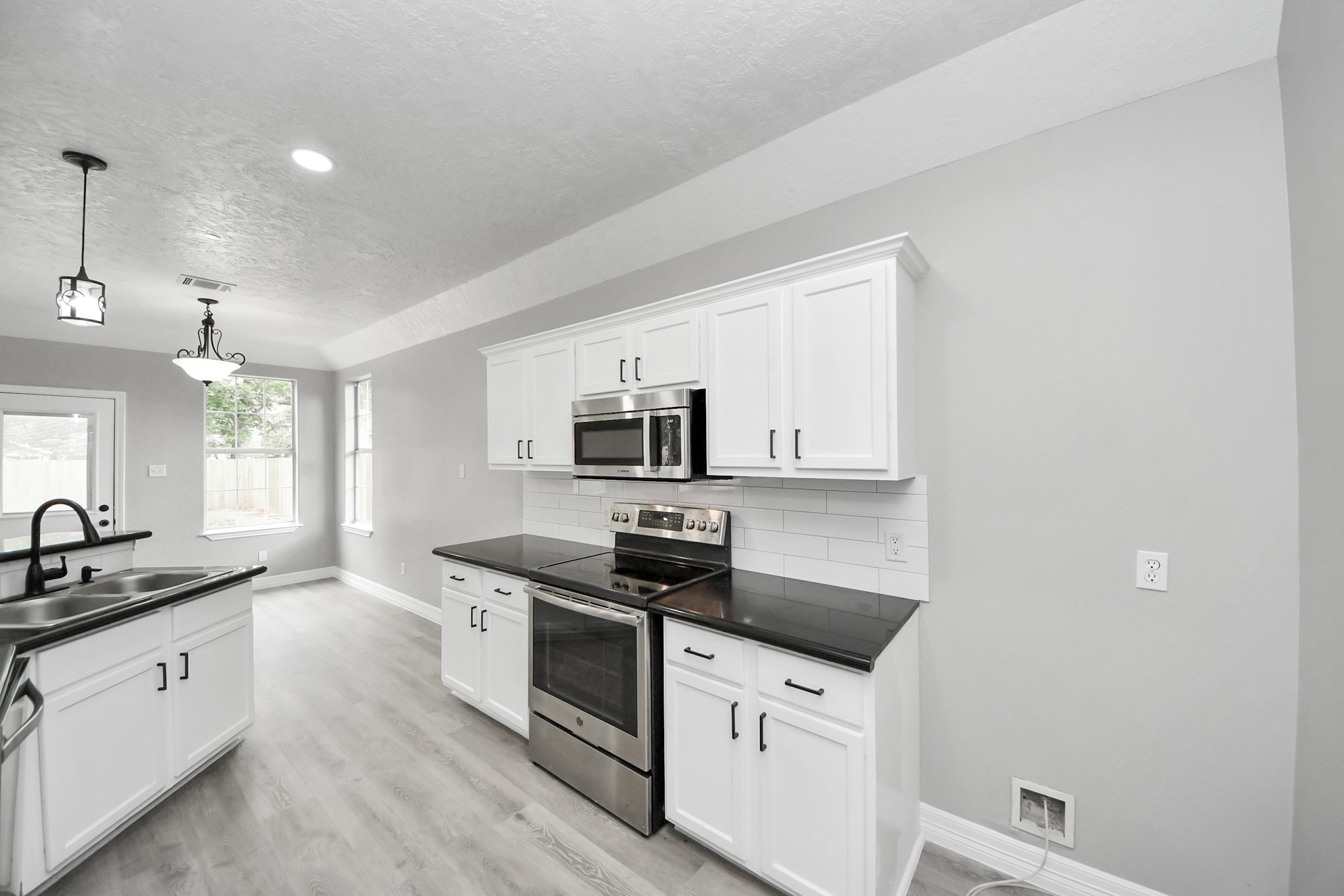 1105 East Kyle Road Clute, TX 77531 - Photo 14 of 44 The modern kitchen with sleek black countertops, white cabinetry, and stainless steel appliances, including a stove and microwave.