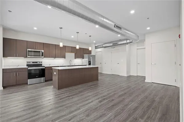 a large kitchen with stainless steel appliances a large counter top a stove a sink dishwasher and a refrigerator with wooden floor