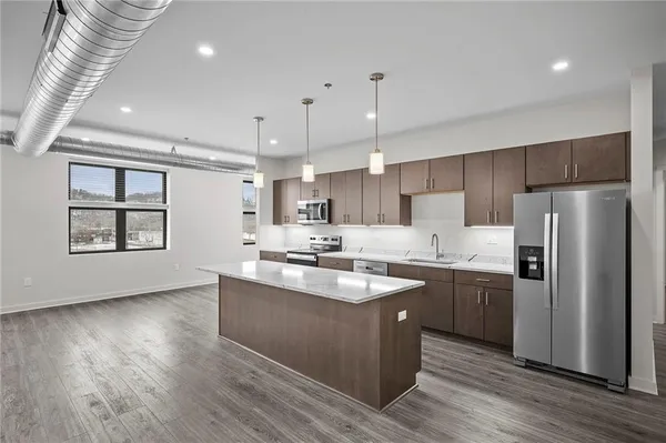 a kitchen with stainless steel appliances granite countertop a sink a stove a refrigerator and island with wooden floors