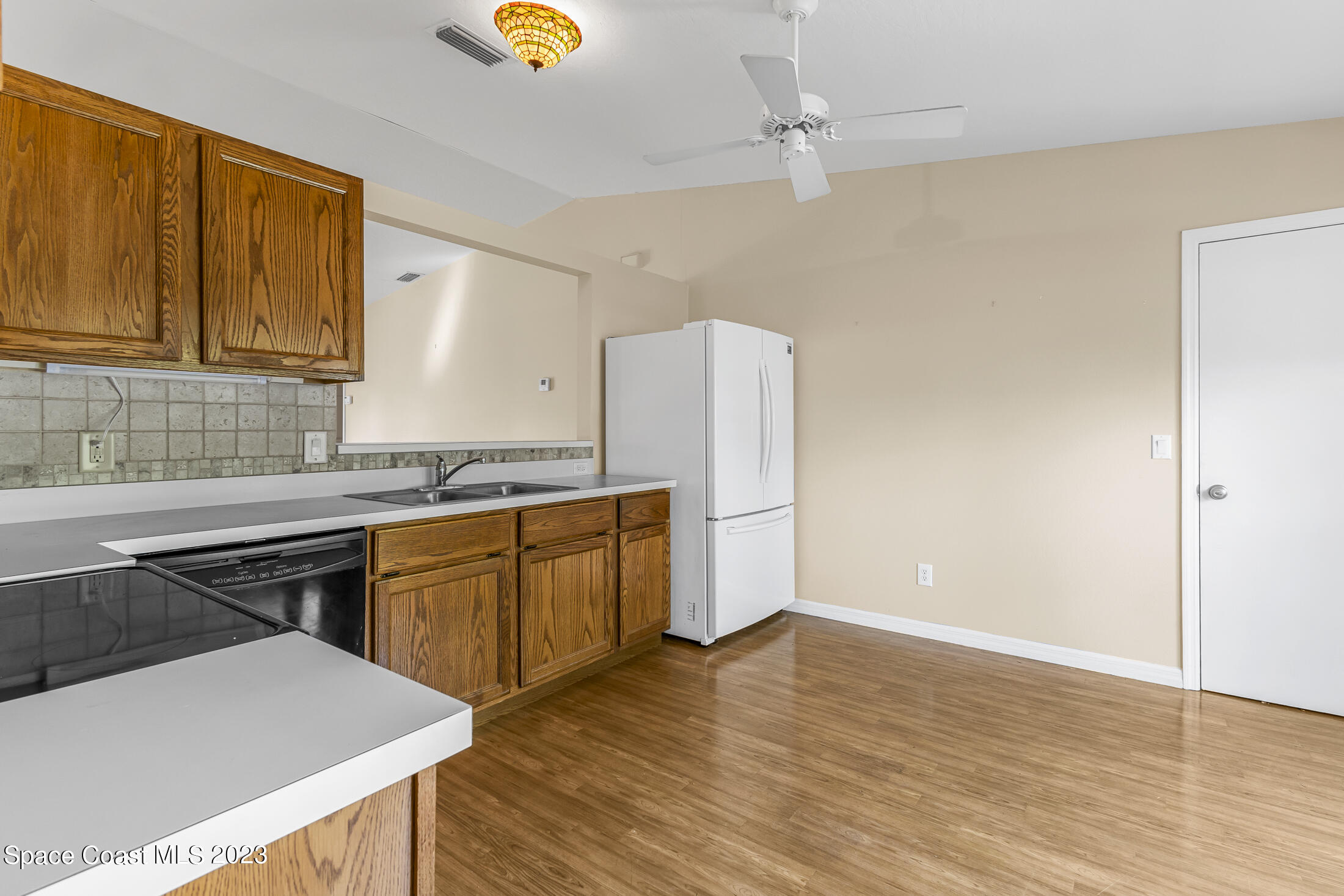 813 Cebu Place Melbourne, FL 32940 - Photo 5 of 25 a kitchen with granite countertop a refrigerator a sink dishwasher and wooden cabinets with wooden floor