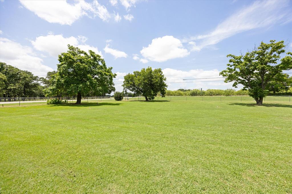 4210 Waples Road Granbury, TX 76049 - Photo 5 of 37 Expansive green lawn with mature trees and a chain-link fence