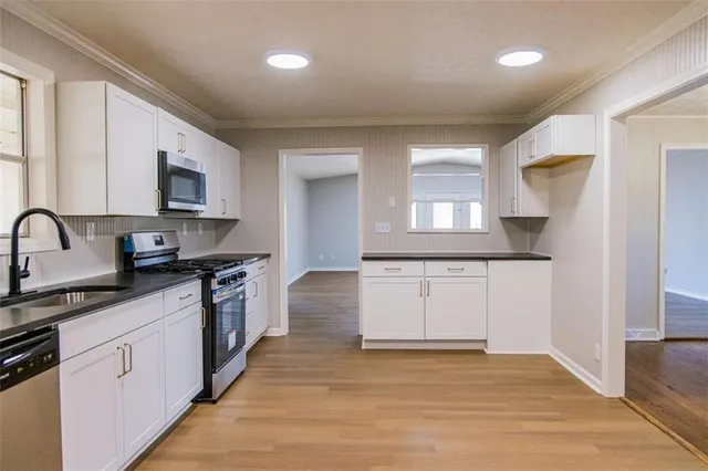 a large kitchen with granite countertop a stove top oven a sink dishwasher and white cabinets with wooden floor