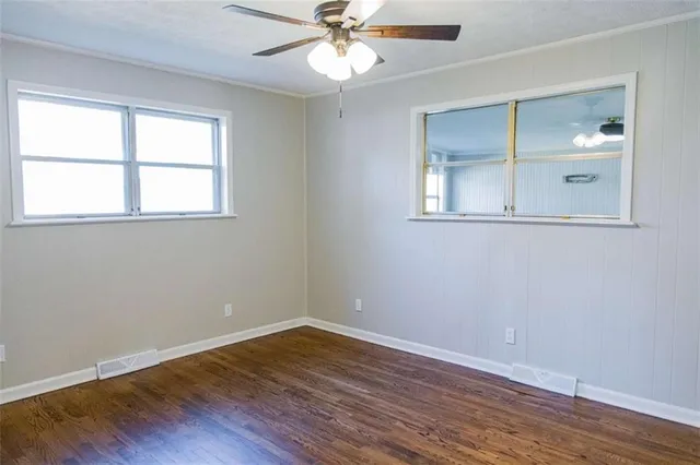 an empty room with wooden floor fan and windows