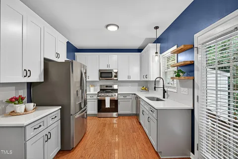 a kitchen with stainless steel appliances granite countertop a refrigerator a sink dishwasher a oven with white cabinets and wooden floor