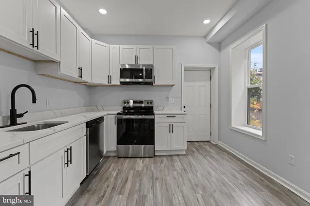 a kitchen with stainless steel appliances a sink a stove a refrigerator cabinets and a window