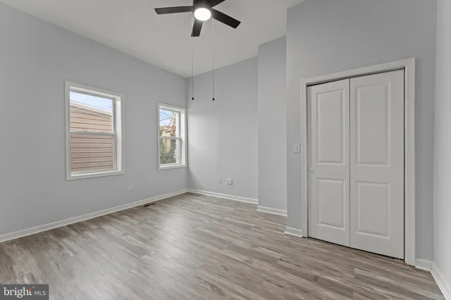 an empty room with wooden floor chandelier fan and windows