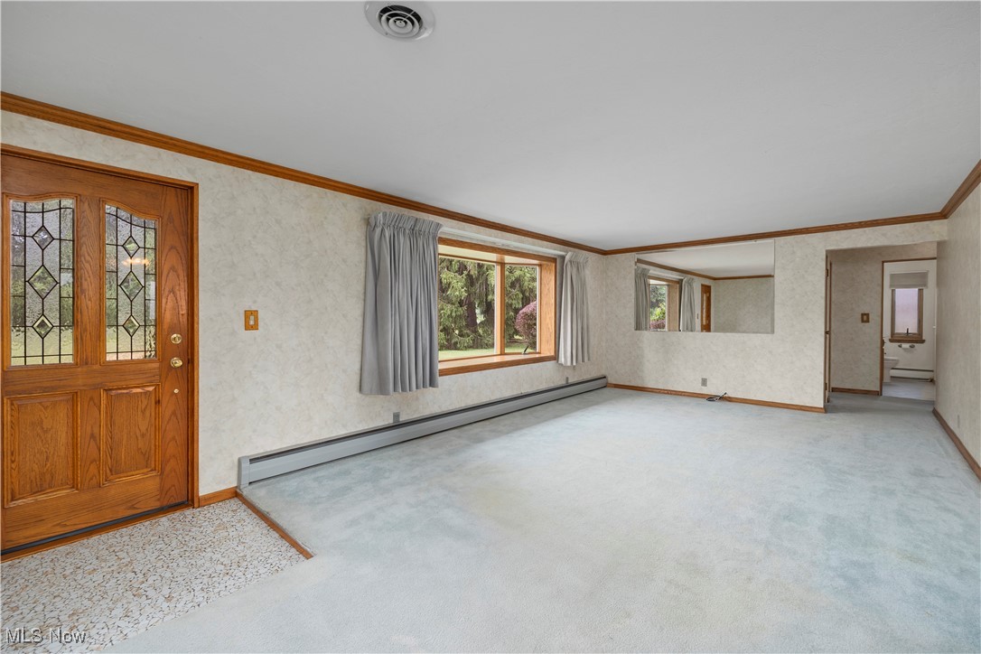 Carpeted foyer entrance featuring a baseboard radiator, crown molding, and wallpapered walls