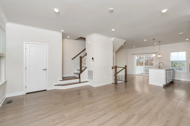 a view of an empty room with wooden floor and a kitchen