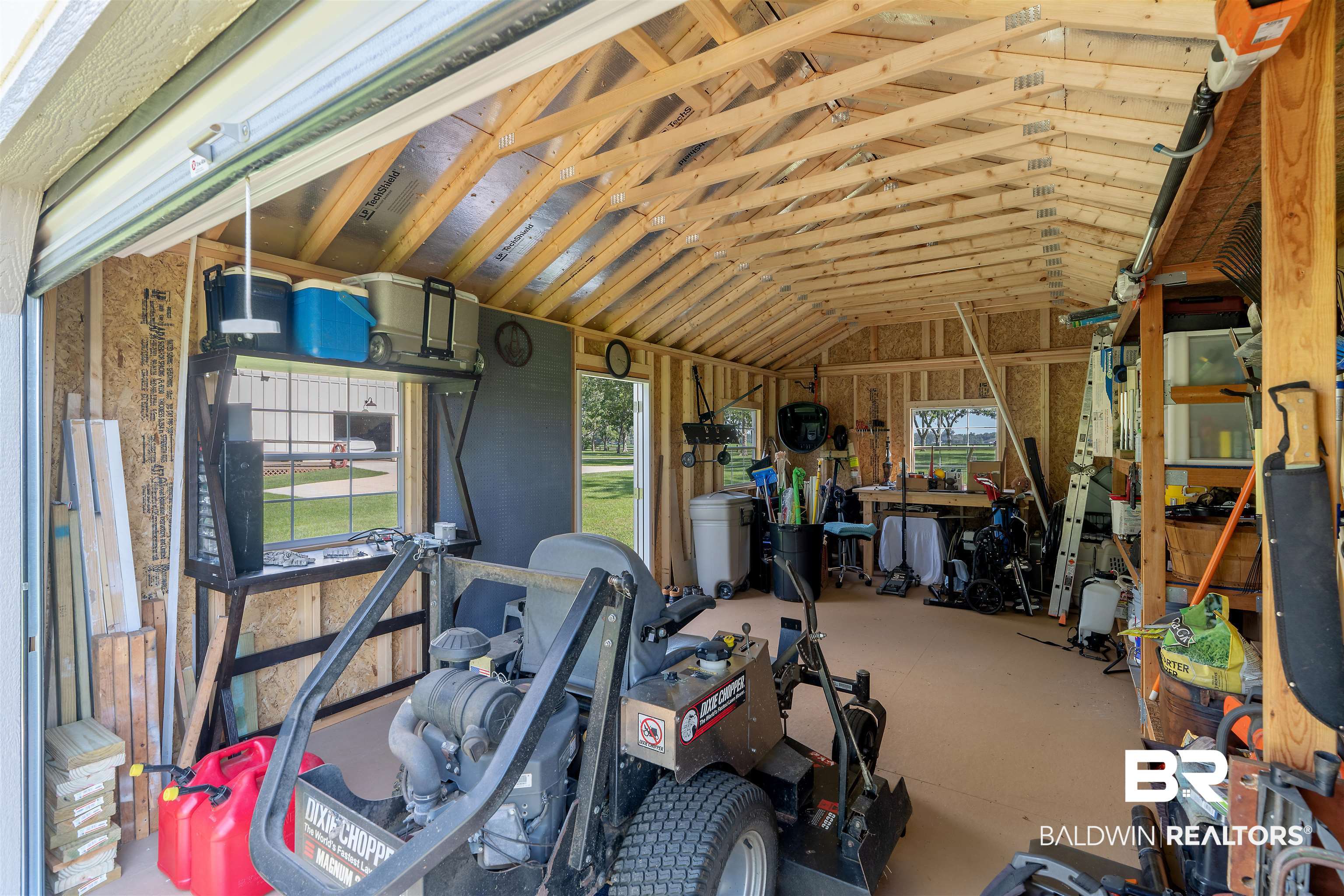 8753 Bishop Road Fairhope, AL 36532 - Photo 49 of 59 Spacious utility building featuring an exposed wood truss ceiling, raw plywood walls, and a large roll-up door