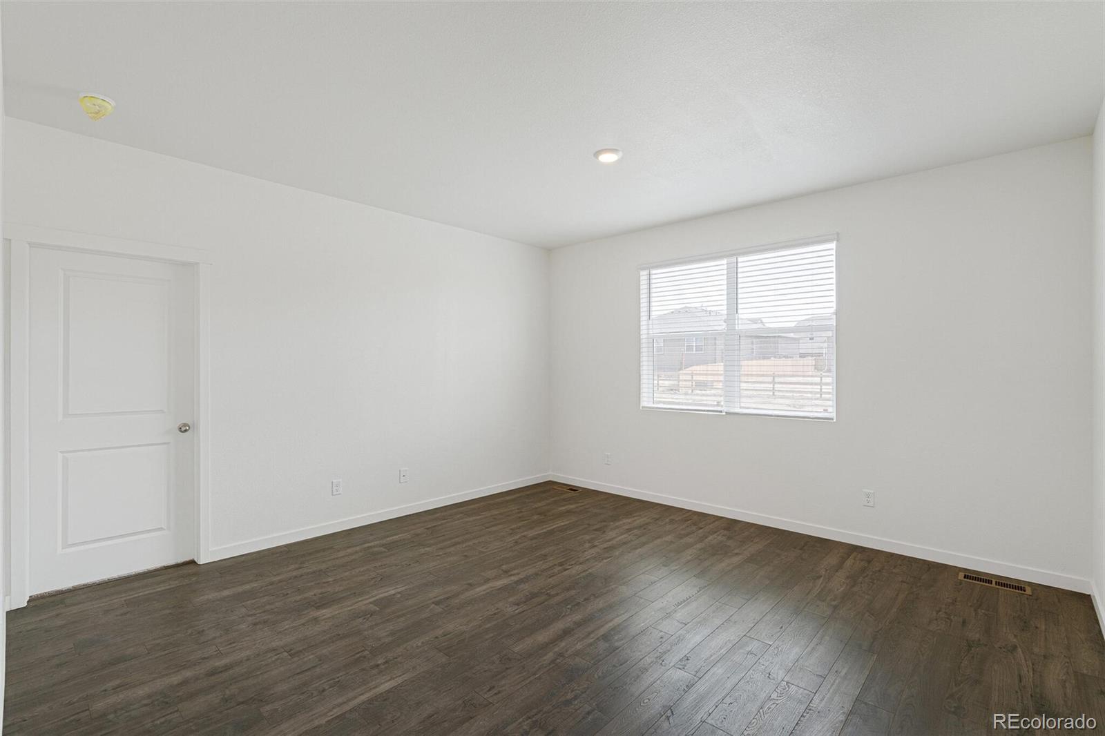 522 Twilight Court Fort Lupton, CO 80621 - Photo 6 of 29 an empty room with wooden floor and windows