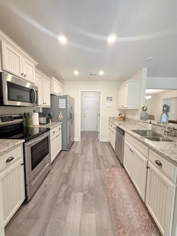 a large kitchen with stainless steel appliances granite countertop a large stove a sink dishwasher a refrigerator with white cabinets and wooden floor