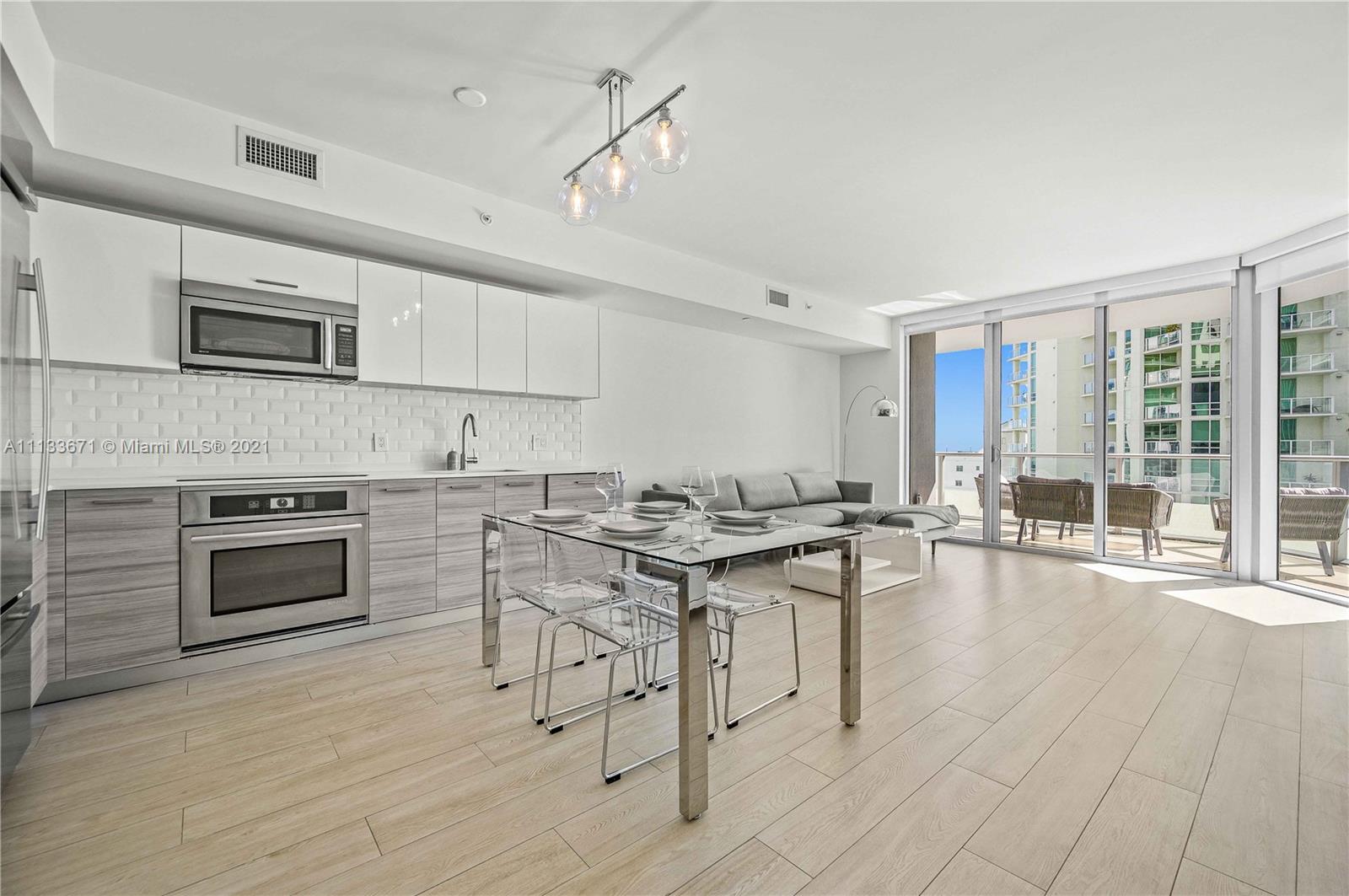 1300 Brickell Bay Drive, Unit 1603 Miami, FL 33131 - Photo 12 of 32 a kitchen with stainless steel appliances kitchen island granite countertop a stove top oven a sink a dining table and chairs with wooden floor