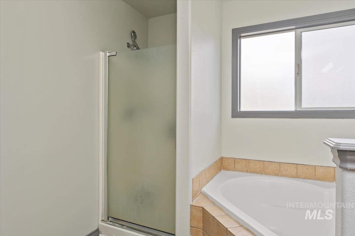 80 Cobblestone Court Middleton, ID 83644 - Photo 24 of 48 Bathroom featuring a built-in corner soaking tub with tile surround, a shower with a frosted glass enclosure, and a sliding window with gray trim