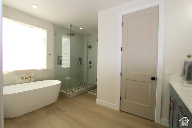 2201 East Unity Way Eagle Mountain, UT 84005 - Photo 20 of 39 Freestanding soaking tub, glass-enclosed shower with pebble flooring, light wood-finish flooring, and a vanity with a white countertop