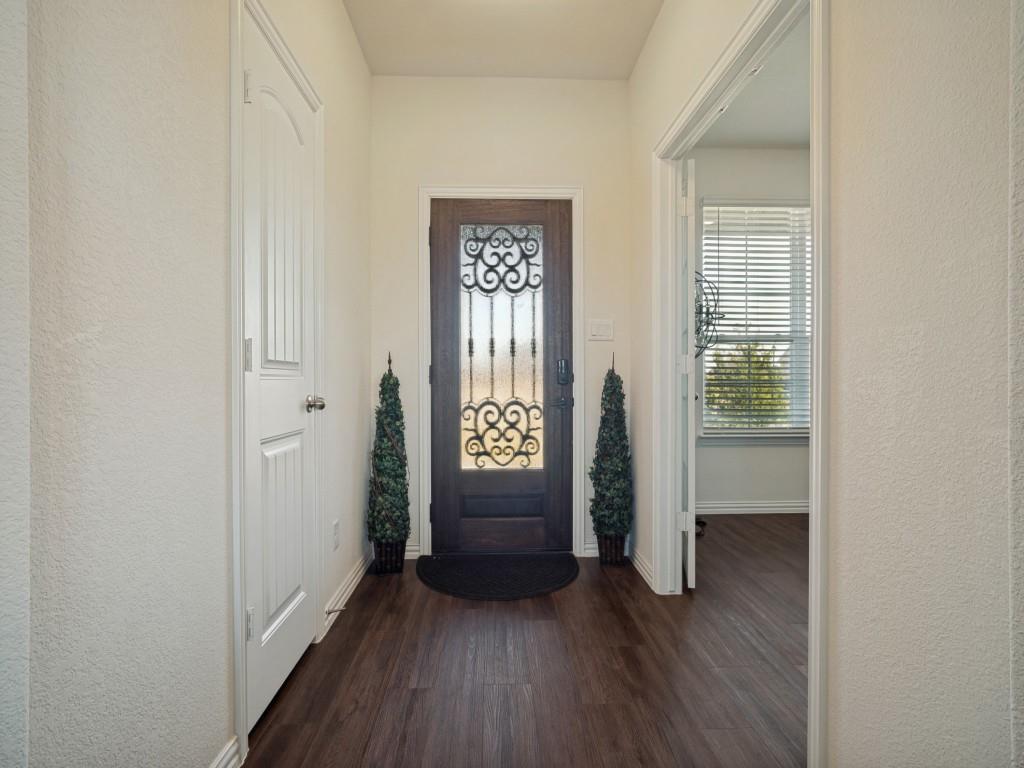 Dark wood-finish flooring, white painted walls, and a decorative front door with an ornate wrought iron insert