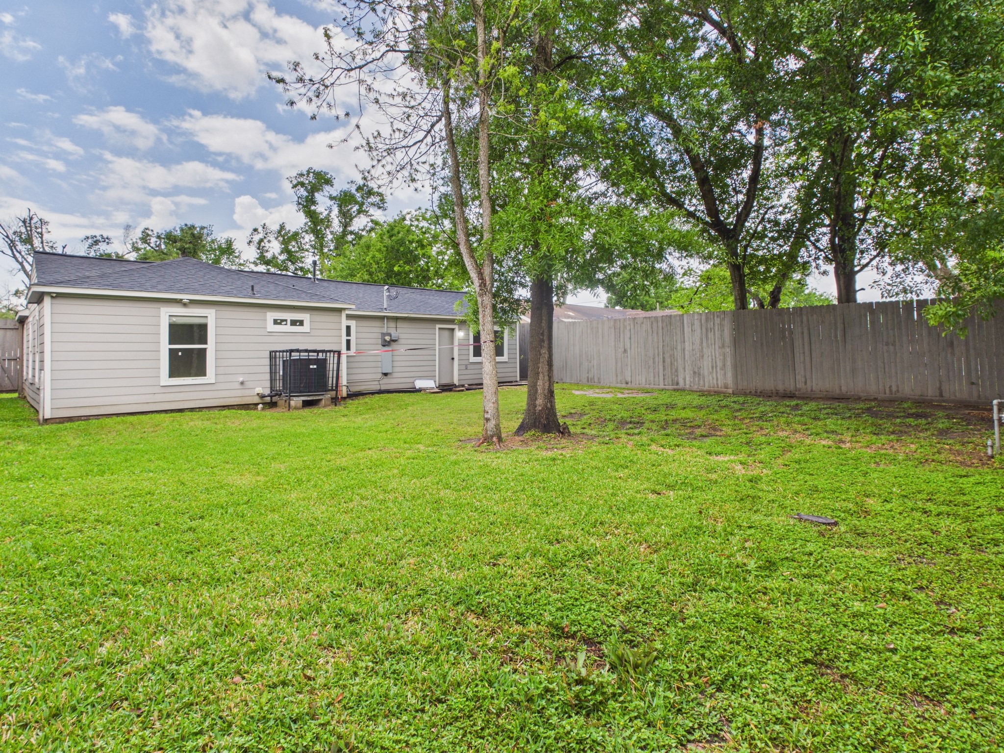 4927 Kelso Street Houston, TX 77021 - Photo 40 of 45 Spacious backyard with well-maintained lawn, mature trees, and privacy fence, adjacent to a one-story home with light gray siding. Ideal for outdoor activities and relaxation.