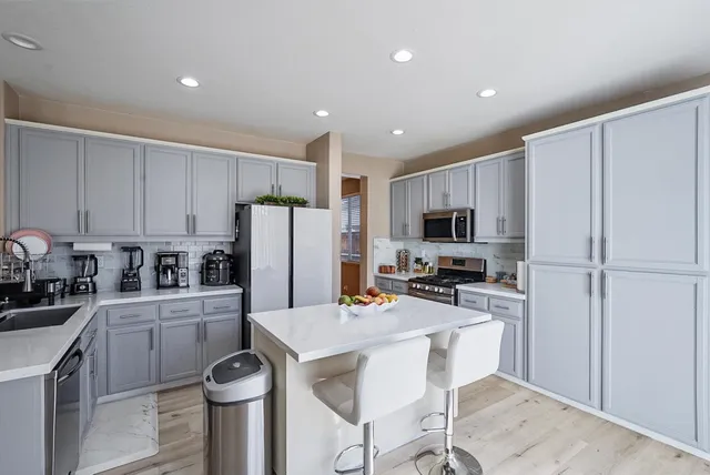 a kitchen with granite countertop a refrigerator stove a sink and white cabinets with wooden floor