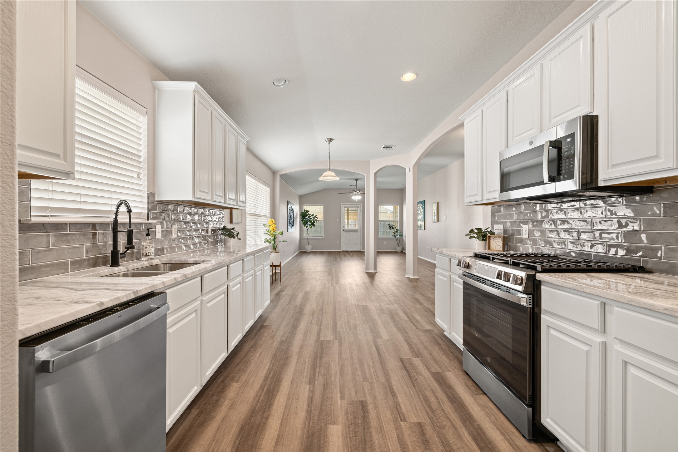 Kitchen with stainless steel appliances, decorative backsplash, arched walkways, hanging light fixtures, and white cabinetry