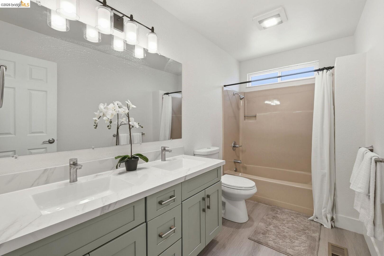 1590 Sunset Road Brentwood, CA 94513 - Photo 26 of 45 Bathroom featuring a double vanity with light green cabinetry and white countertops, a large framed mirror, a bathtub with an integrated shower, and wood-finish flooring