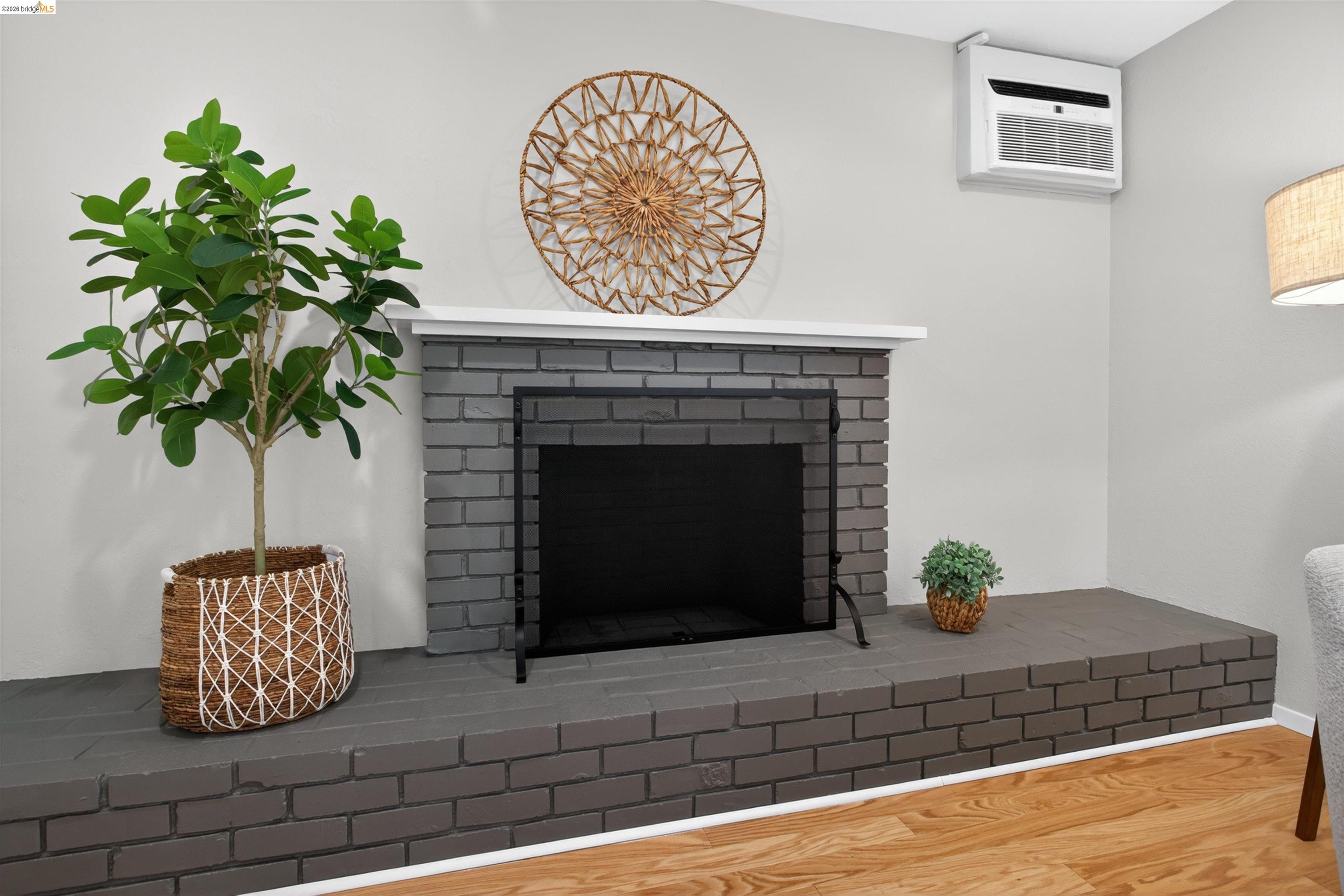 4321 Davis Way Livermore, CA 94550 - Photo 17 of 34 Painted brick fireplace with a white mantel and black fire screen, complemented by light wood-finish flooring and a wall-mounted air conditioning unit