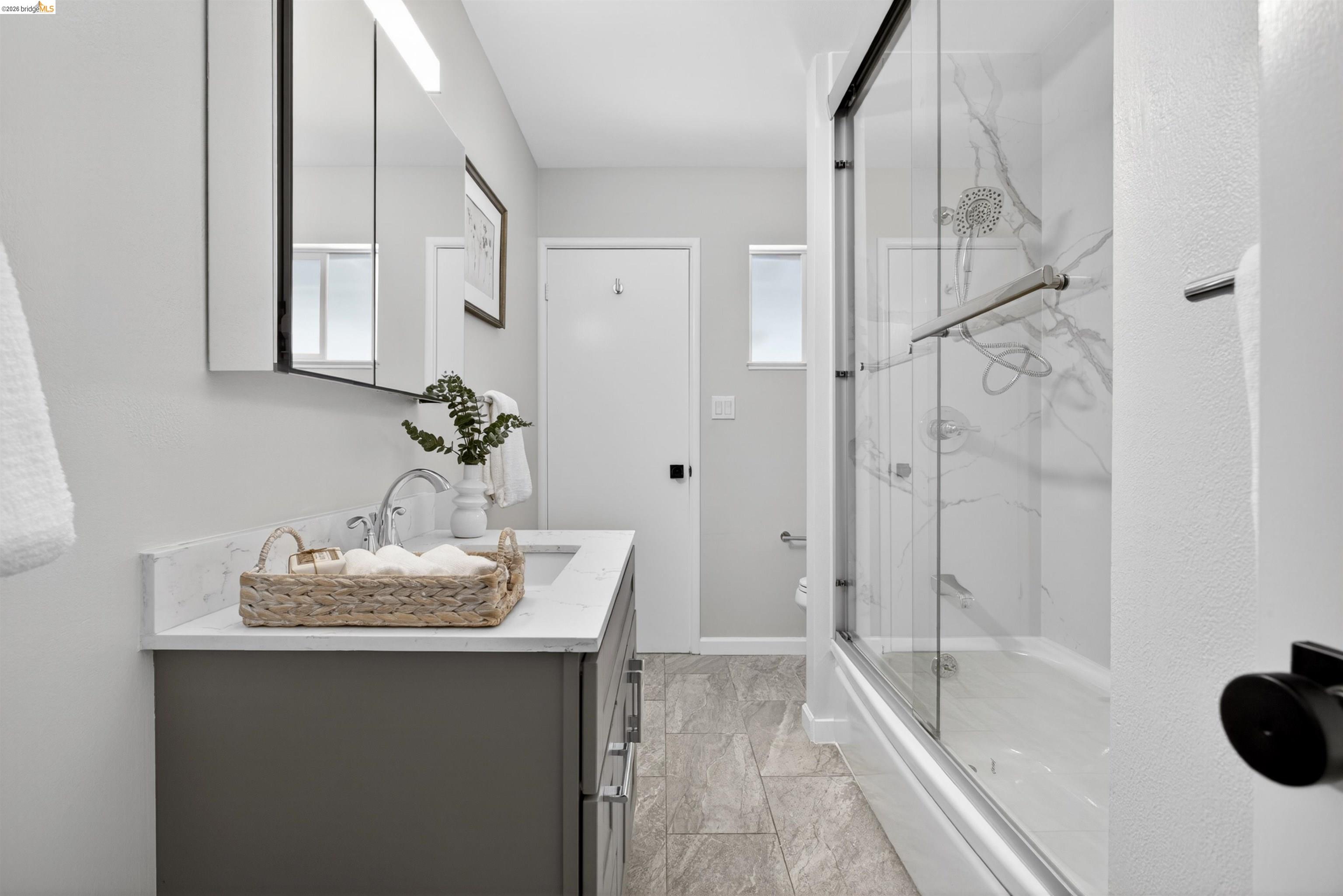 4321 Davis Way Livermore, CA 94550 - Photo 18 of 34 Bathroom featuring a vanity with a white countertop and undermount sink, a framed medicine cabinet, a modern light fixture, a shower-tub combination with a glass enclosure, and stone-finish floor tile