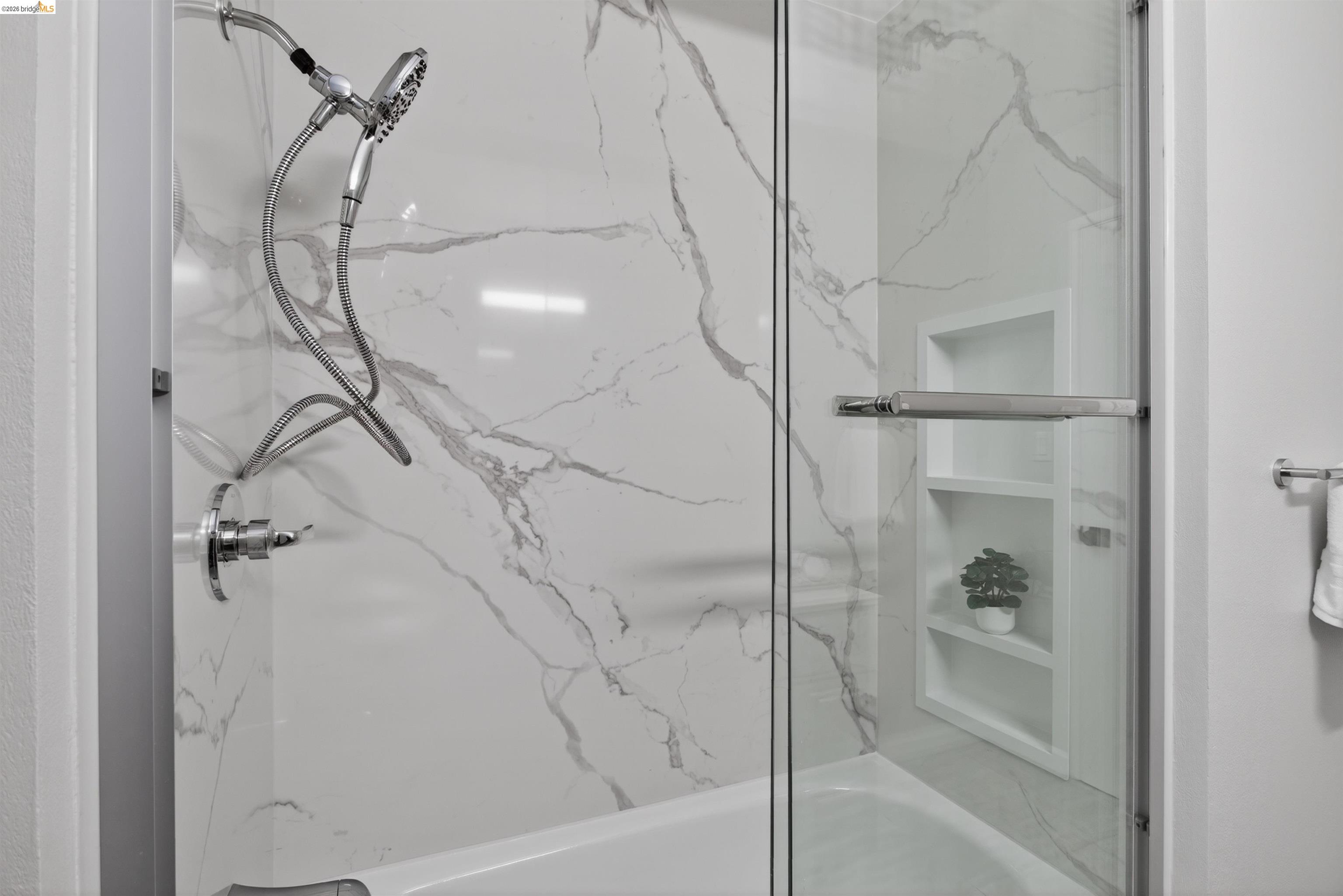 4321 Davis Way Livermore, CA 94550 - Photo 20 of 34 Bathtub and shower combination featuring a glass enclosure, white marble-look shower surround, chrome shower fixtures, and built-in recessed shelving