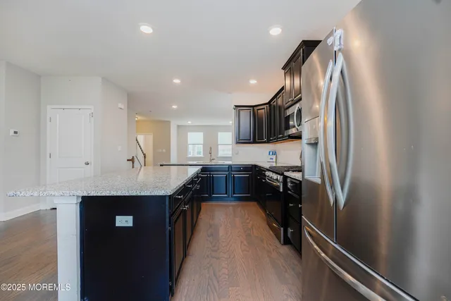a kitchen with kitchen island granite countertop a refrigerator a sink and black cabinets