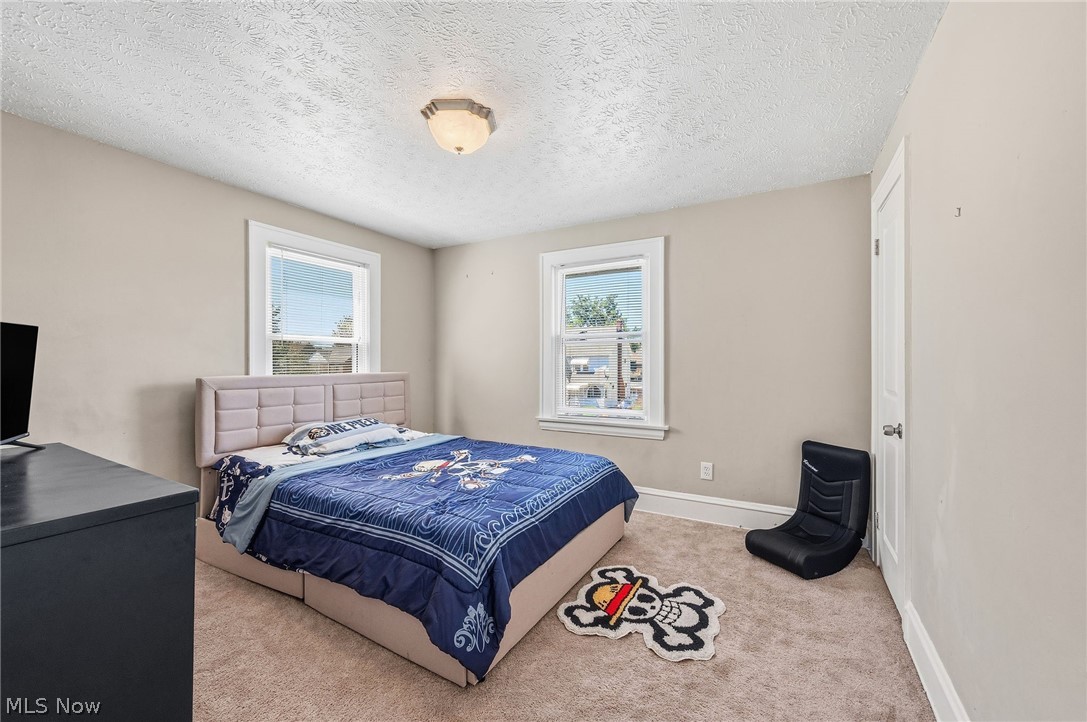 3386 Sylvanhurst Road Cleveland Heights, OH 44112 - Photo 20 of 46 Bedroom featuring two windows with white trim, light beige wall paint, textured ceiling, and neutral-toned carpeting