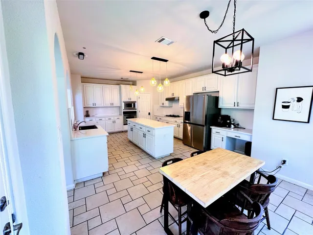 a kitchen with stainless steel appliances kitchen island granite countertop a refrigerator a stove a sink dishwasher and white cabinets with wooden floor
