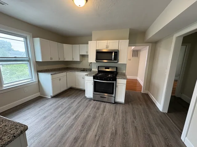 a kitchen with stainless steel appliances a stove a sink a microwave a refrigerator a window and wooden floor