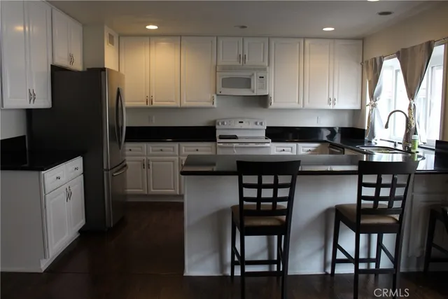 a kitchen with stainless steel appliances granite countertop a stove a sink a refrigerator with white cabinets and wooden floor