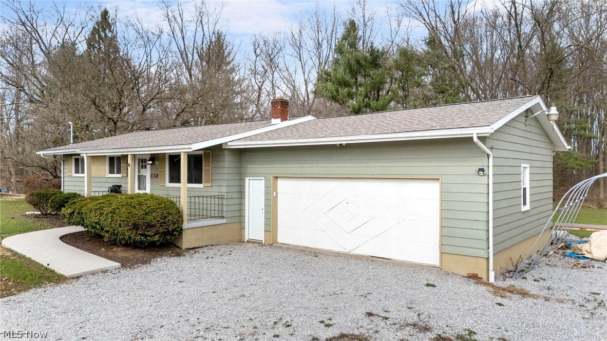 Ranch-style home featuring a chimney, a shingled roof, an attached garage, and gravel driveway
