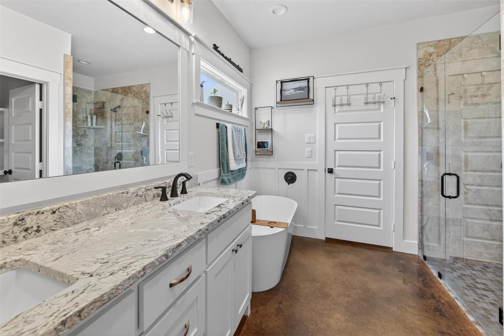 6371 Mill Run Road Athens, TX 75751 - Photo 15 of 40 Contemporary bathroom featuring a spacious vanity with a light-toned granite countertop and two sinks, a freestanding soaking tub, and a glass-enclosed shower