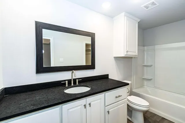 a bathroom with a granite countertop sink a toilet and a mirror