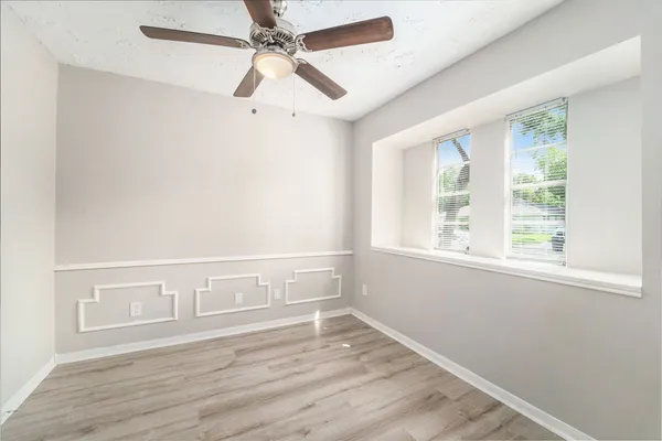 an empty room with wooden floor fan and windows