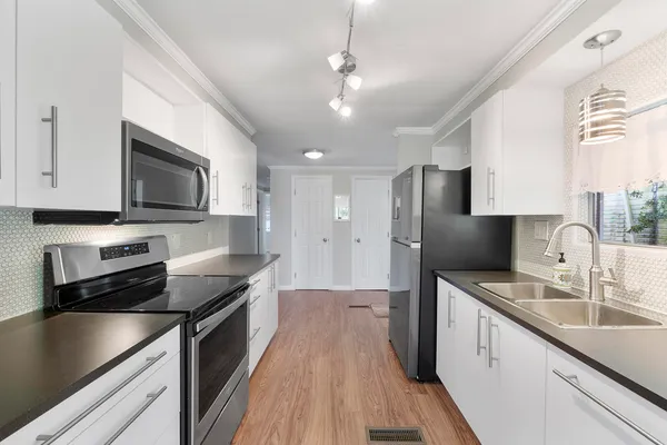 a kitchen with stainless steel appliances a sink dishwasher a stove top oven a refrigerator with white cabinets and wooden floor