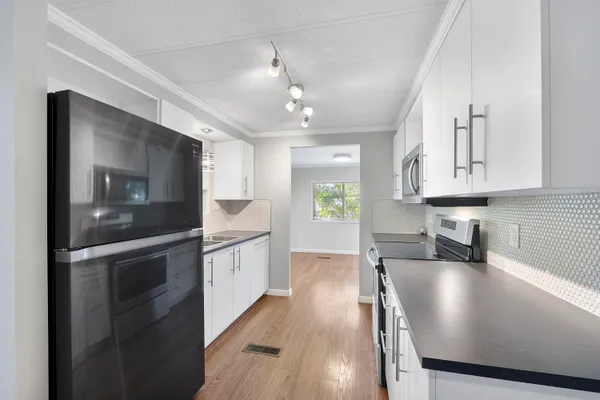 a kitchen with stainless steel appliances granite countertop a stove a refrigerator a sink a microwave oven with white cabinets and wooden floor