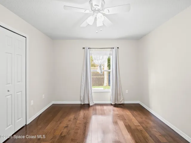 an empty room with wooden floor chandelier fan and windows