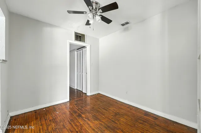 a view of an empty room with wooden floor and a ceiling fan