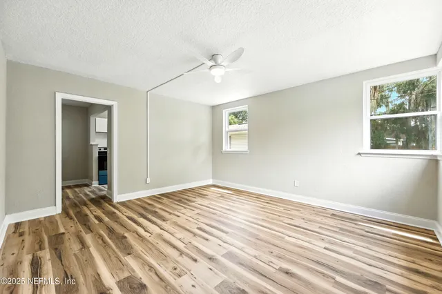 a view of an empty room with wooden floor and a ceiling fan