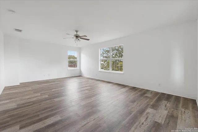 an empty room with wooden floor chandelier fan and windows