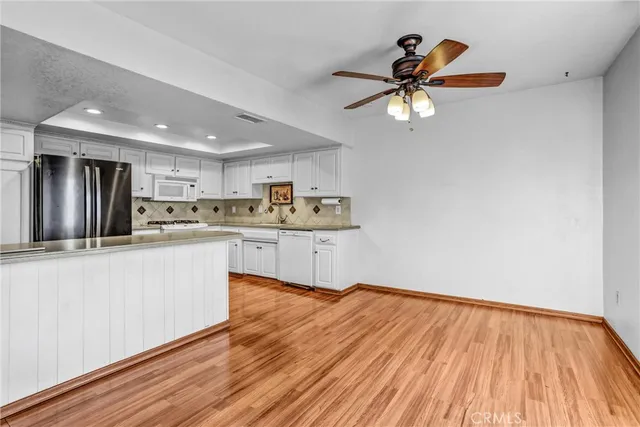 a kitchen with stainless steel appliances granite countertop a refrigerator a sink dishwasher a stove and white countertops with wooden floor