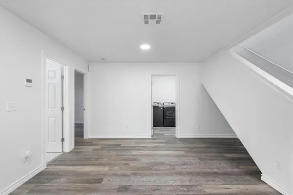 an empty room with wooden floor kitchen view and a window