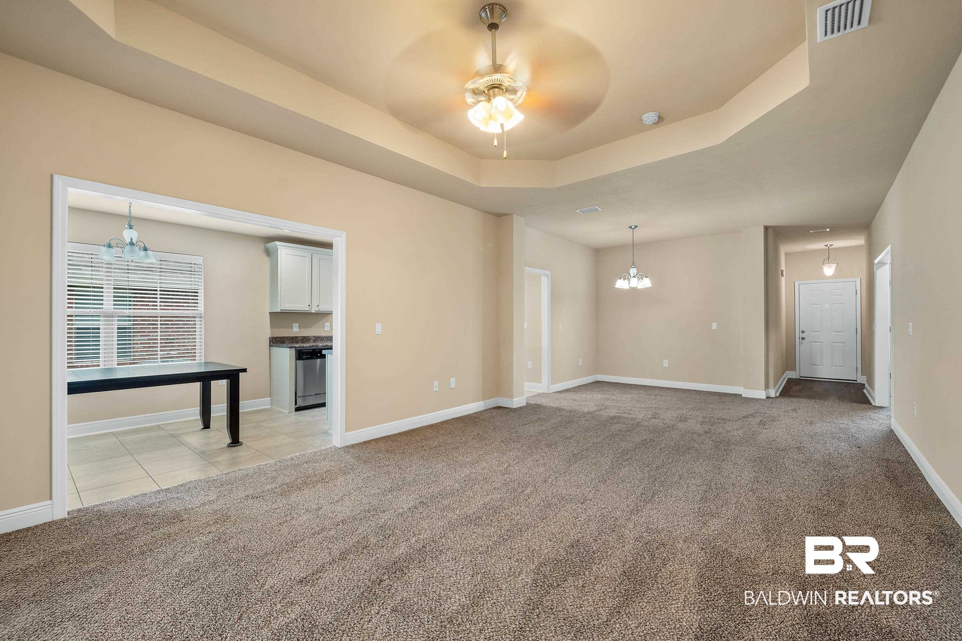22631 Lake South Drive Foley, AL 36535 - Photo 7 of 25 Unfurnished living room featuring light carpet, a tray ceiling, and ceiling fan with notable chandelier