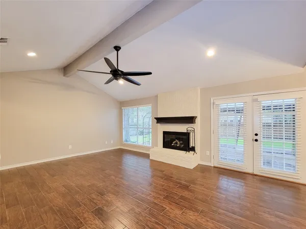 an empty room with wooden floor fireplace and windows