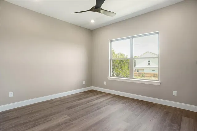 an empty room with wooden floor chandelier fan and windows