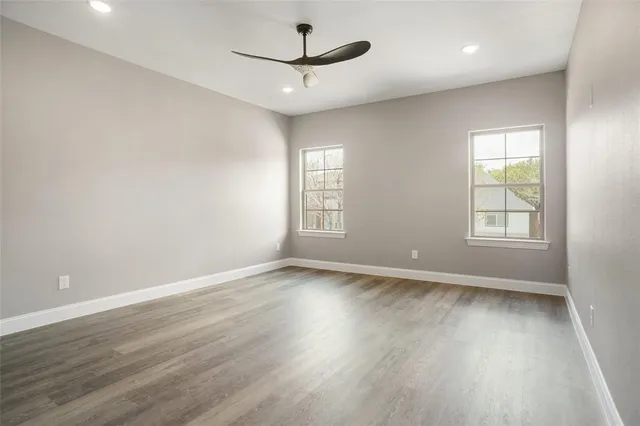 an empty room with wooden floor ceiling fan and windows